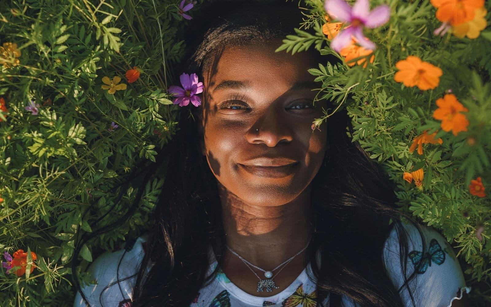 young black woman laying in grass with flowers around her head